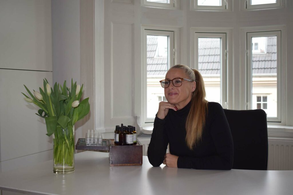 Kvinde smilende briller klaedt i sort sidder foran desk pa kontoret
