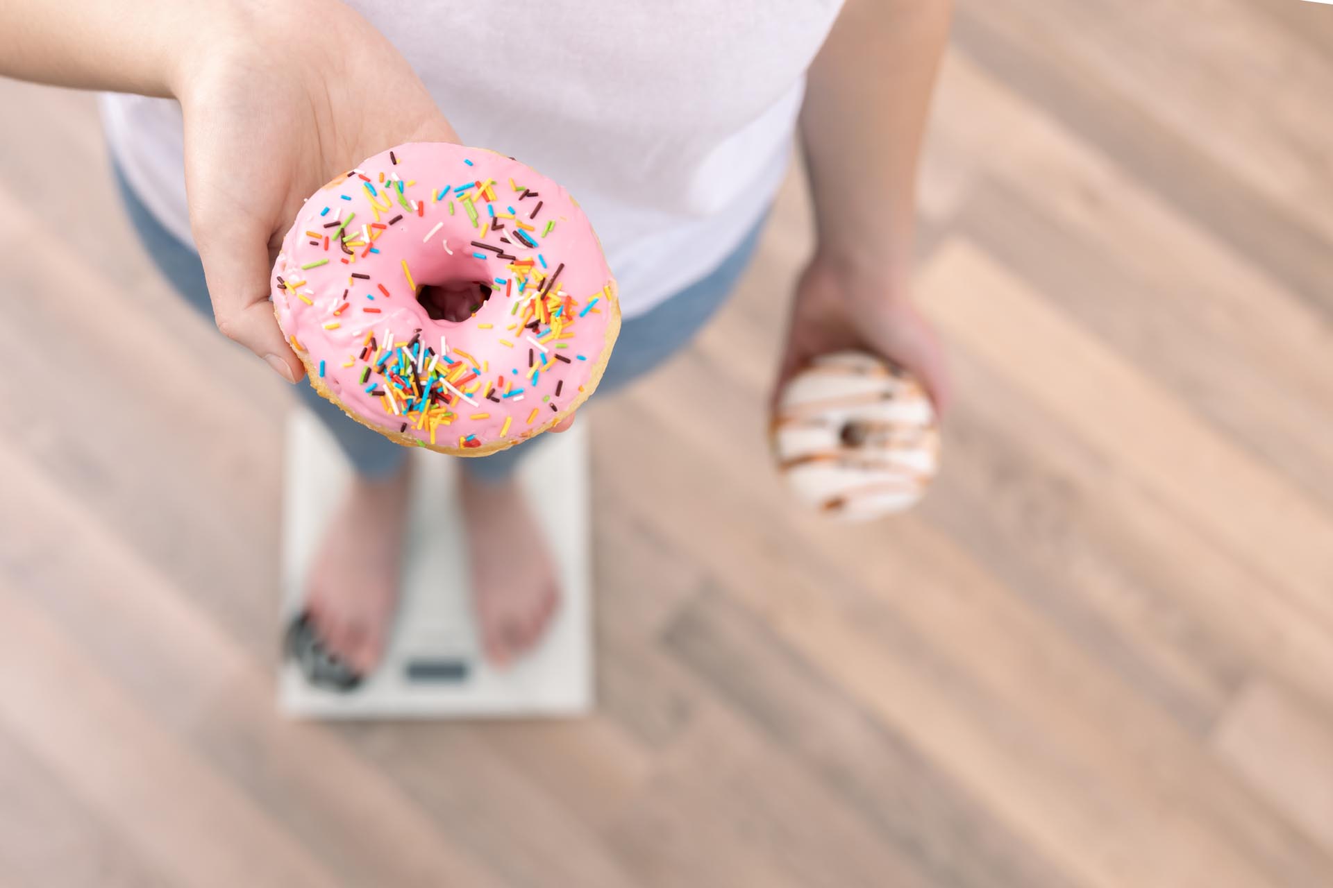 A woman stands on the scales, holds donuts in her hands, top view, copy space.