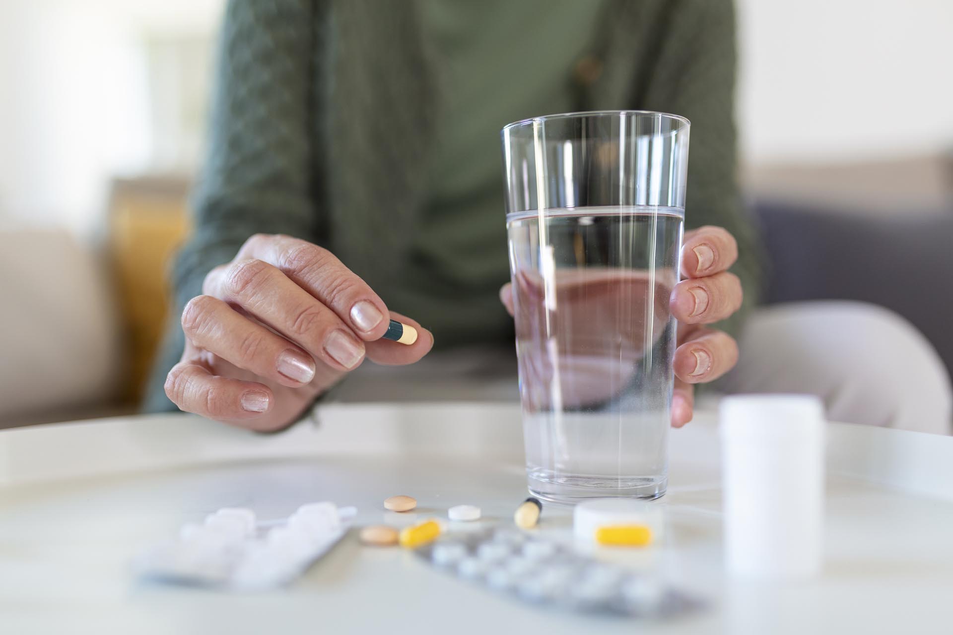 Senior woman takes pill with glass of water in hand.
